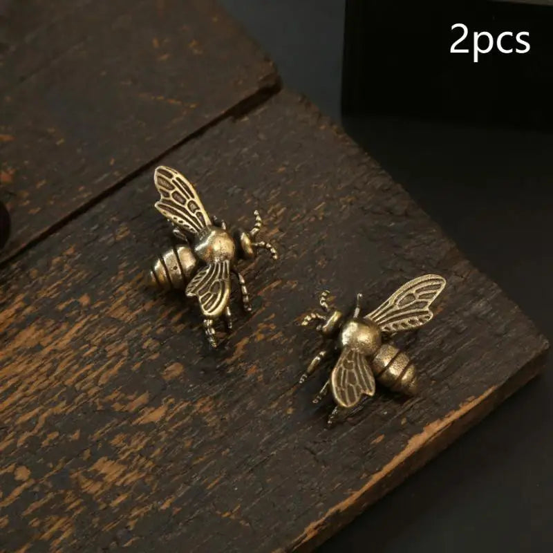 Deux figurines de guêpes en laiton vintage posées sur une surface en bois sombre.