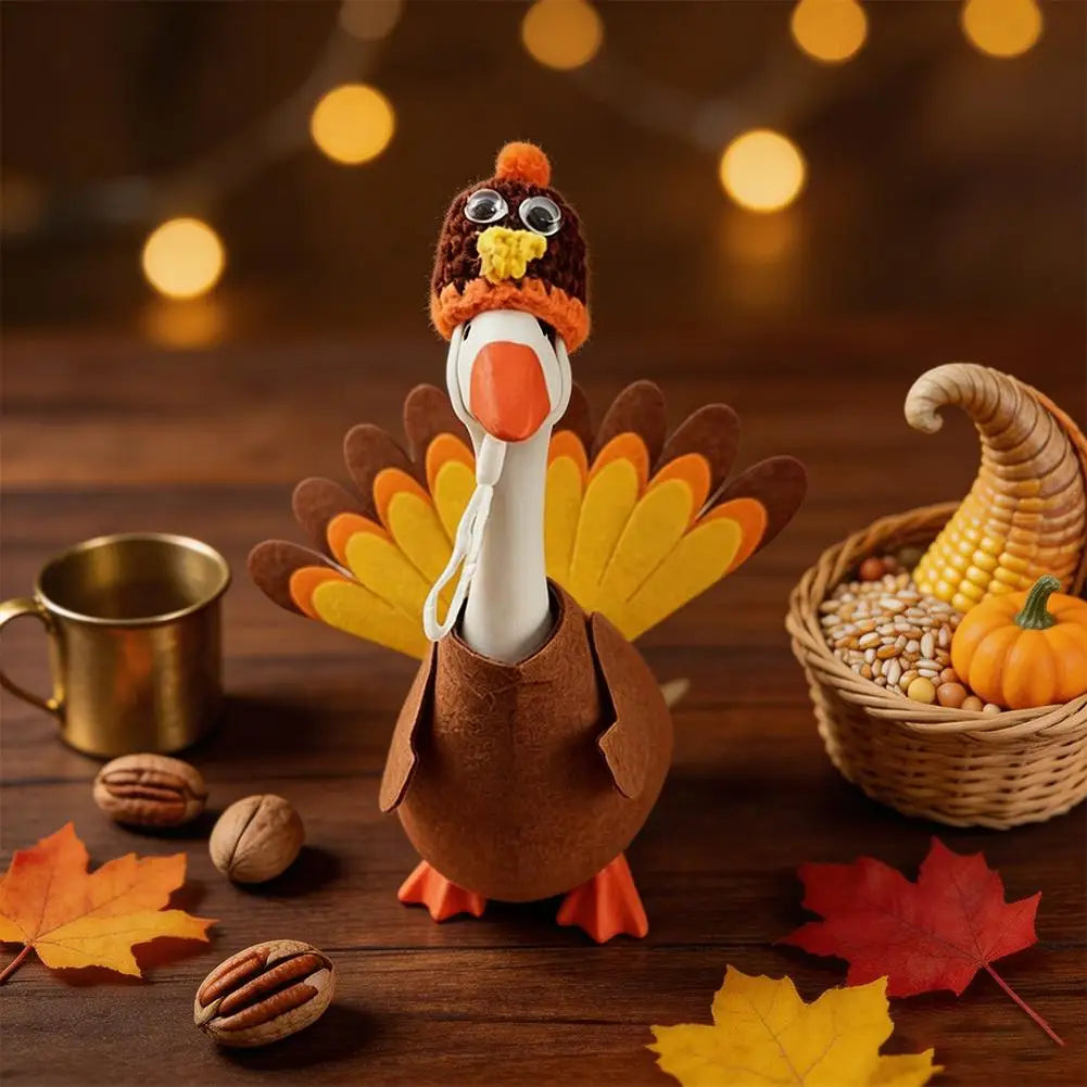 A felt turkey costume shaped like a goose statue is displayed on a wooden surface with autumn leaves and corn.