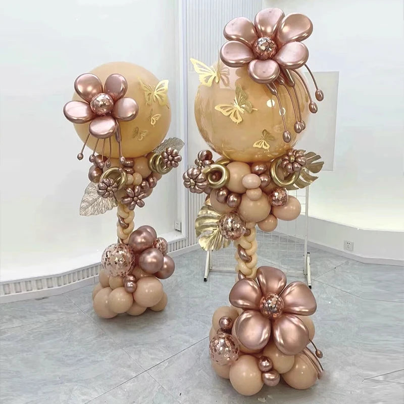 A display of pink and gold metallic balloons arranged in a column stand with floral accents.