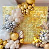 A golden glitter square wall backdrop decorated with clusters of gold and silver balloons.