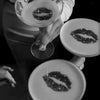 A person holds a glass and a plate, both featuring an artistic representation of lips made from dark specks.
