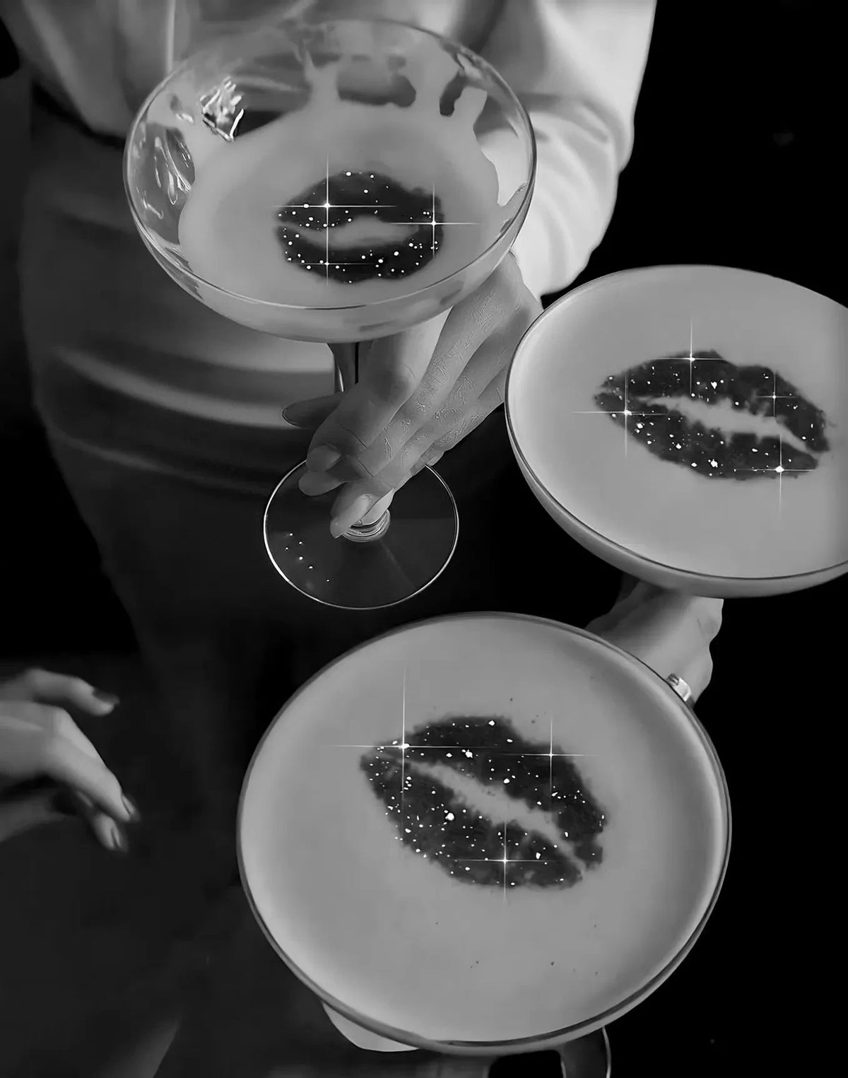 A person holds a glass and a plate, both featuring an artistic representation of lips made from dark specks.
