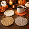 A set of four handmade crochet pumpkin coasters in various natural tones arranged on a wooden surface.