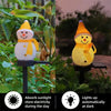 A yellow solar powered outdoor christmas snowman light illuminating a garden setting.