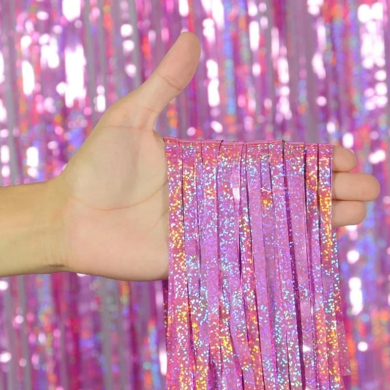 A hand holds a set of metallic pink and purple foil tinsel fringe streamers against a sparkly backdrop.