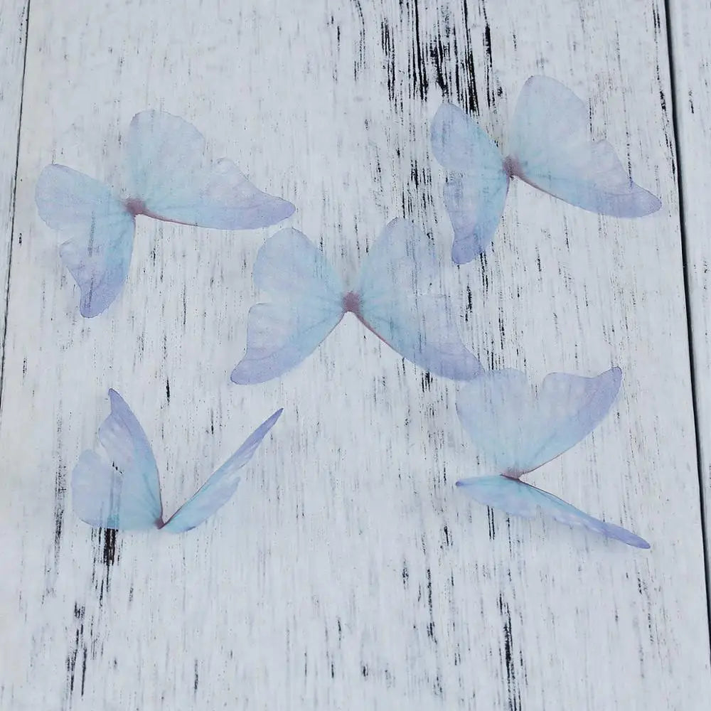 Light blue organza butterfly embellishments scattered on a white wooden surface.