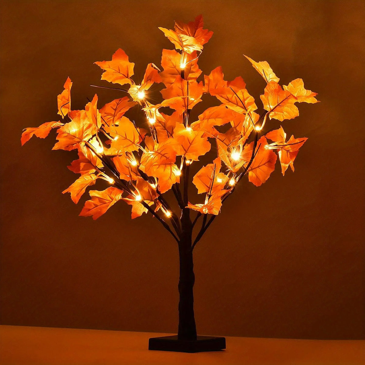Warm glow maple tree decoration with autumn leaves illuminated by lights on a black stand