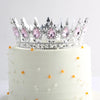 Gâteau à étages blanc décoré d'une couronne en métal scintillant avec des gemmes roses.