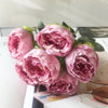 A bouquet of pink silk rose and peony artificial flowers arranged on a white surface.