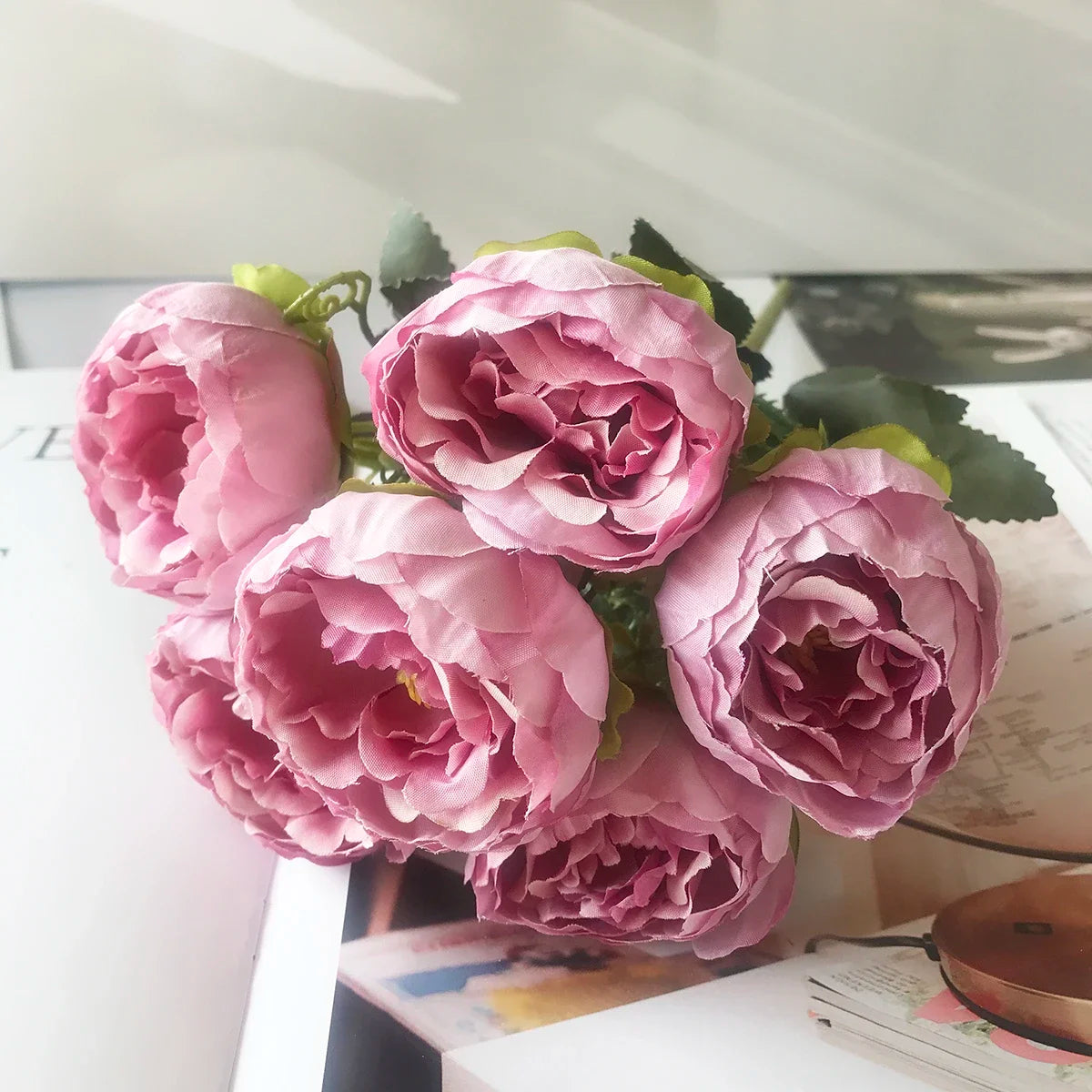 A bouquet of pink silk rose and peony artificial flowers arranged on a white surface.