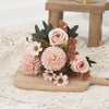 A bouquet of pink and peach roses and hydrangeas with dark green foliage displayed on a wooden board.