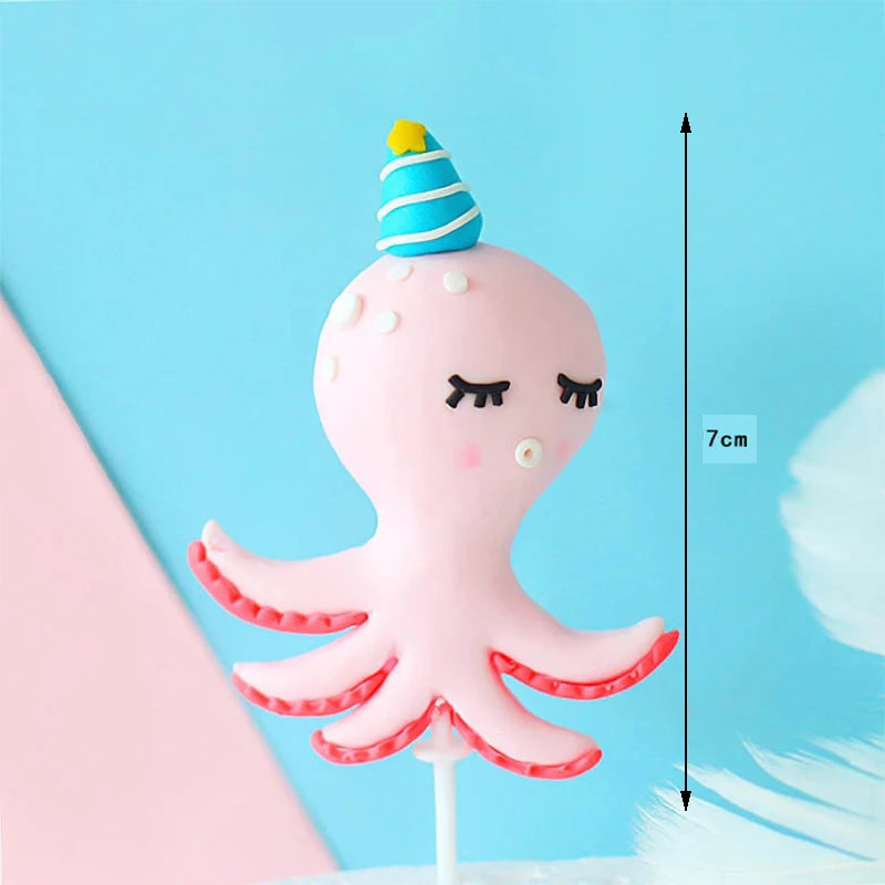 Pink octopus cake topper with tentacles and a yellow conical decoration against a blue background.