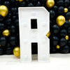 A large white marquee letter R made of acrylic is displayed against a backdrop of black and gold balloons.