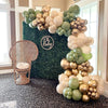 A large arrangement of latex balloons in shades of sage green, gold, and cream decorating a nursery or celebration area.