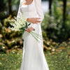 A woman in a white dress holds an artificial delphinium bouquet outdoors.