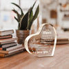 A clear acrylic heart pendant engraved with 'To my mom I love you' resting on a wooden surface.