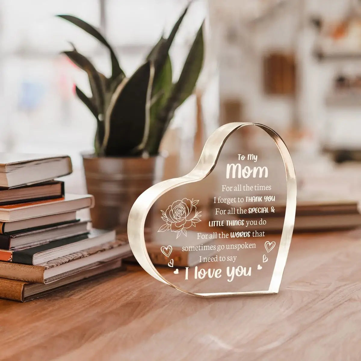A clear acrylic heart pendant engraved with 'To my mom I love you' resting on a wooden surface.