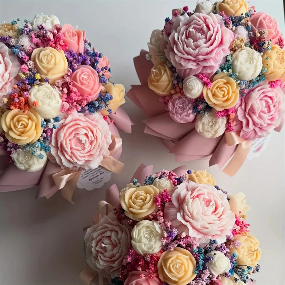 A collection of pink, yellow, and white floral silicone candle molds shaped like roses, peonies, and camellias.