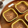 Two square aluminum foil baking boxes filled with chocolate mousse topped with crushed nuts on a wooden tray