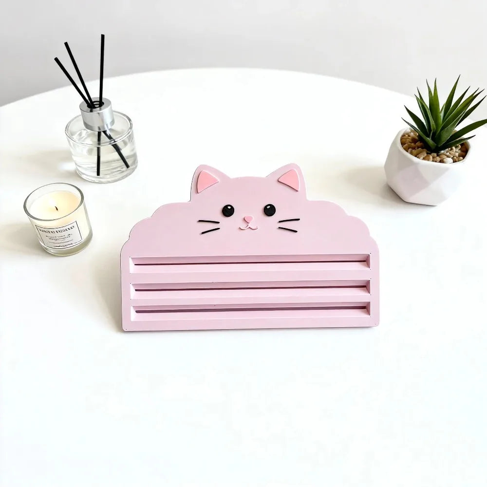 A pink cat-shaped squeezer tool for dispensing cat food, placed on a white surface with a candle and a succulent plant.