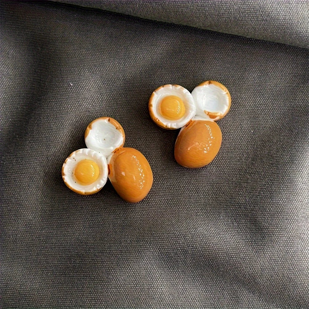 A set of two egg-shaped fridge magnets with yellow centers and white shells resting on a dark gray fabric.