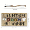 A wooden sign with the text Laundry Room Help Wanted carved into it, featuring hanging clothes and a rope.