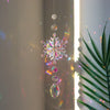 A hanging crystal rainbow wind chime decor featuring a starburst pendant and dangling beads.