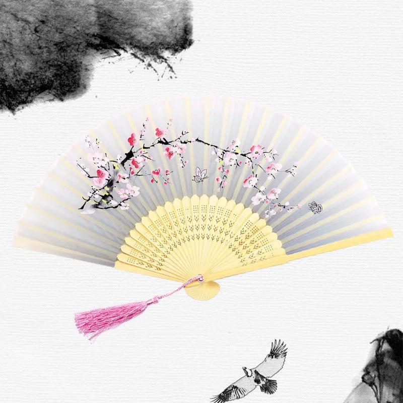 A vintage bamboo folding hand fan with pink flowers and a pink tassel against a white background.