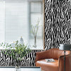A modern interior featuring a brown leather armchair, a glass table, and black and white zebra print wallpaper.