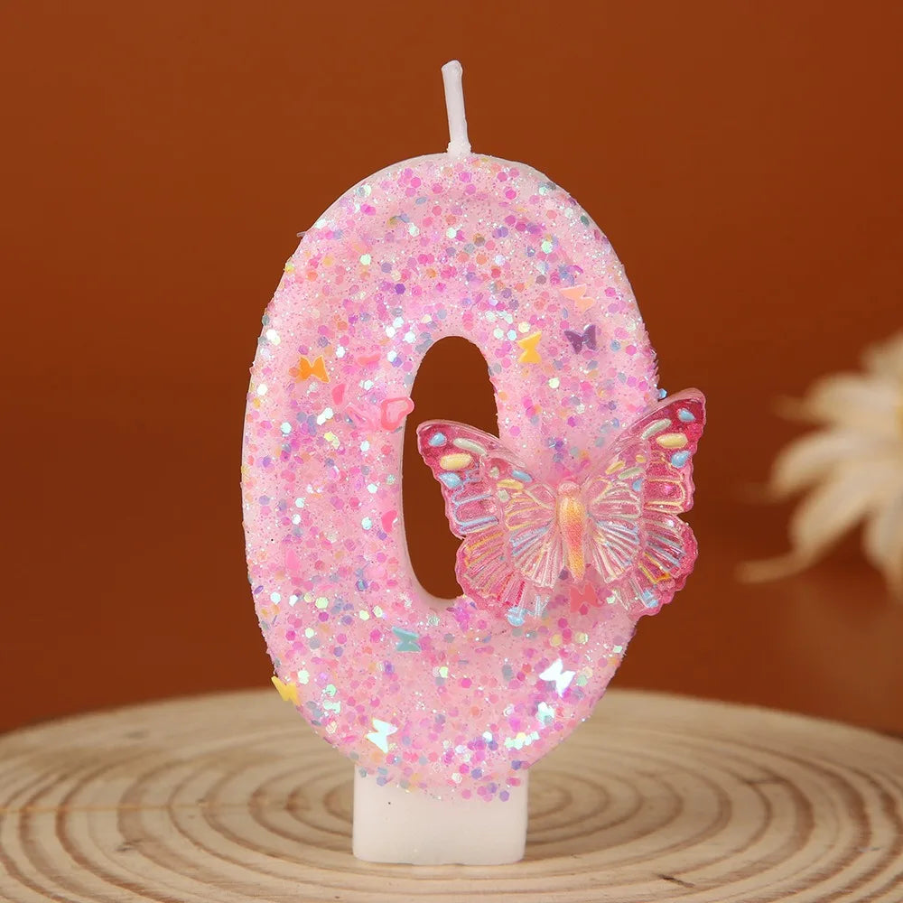 A pink glitter number zero candle decorated with a butterfly shape on a wooden surface.