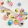A collection of glossy, double-sided eyeball beads in various pinks, greens, and blues for crafting.