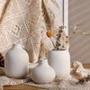 A set of three minimalist white ceramic decorative vases displayed on a textured fabric.