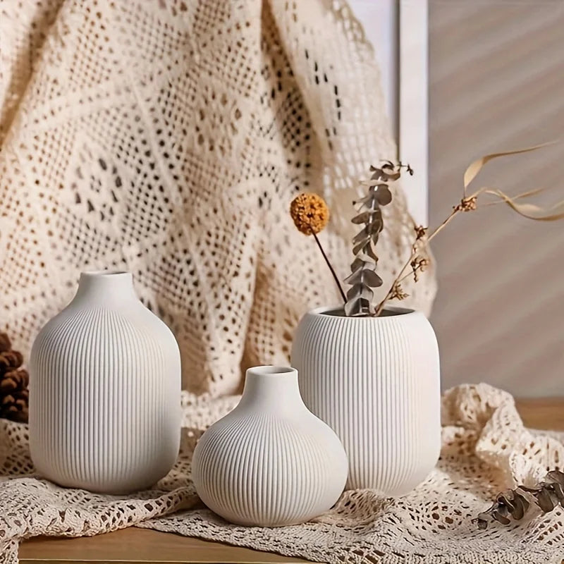 A set of three minimalist white ceramic decorative vases displayed on a textured fabric.