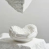 White resin sculpture shaped like an angel wings heart resting on a light gray surface.