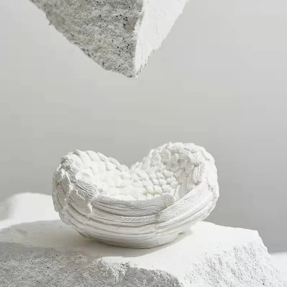 White resin sculpture shaped like an angel wings heart resting on a light gray surface.