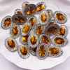 A collection of round, gold-toned gemstone flatback rhinestones set in silver-toned metal, displayed on a white plate.