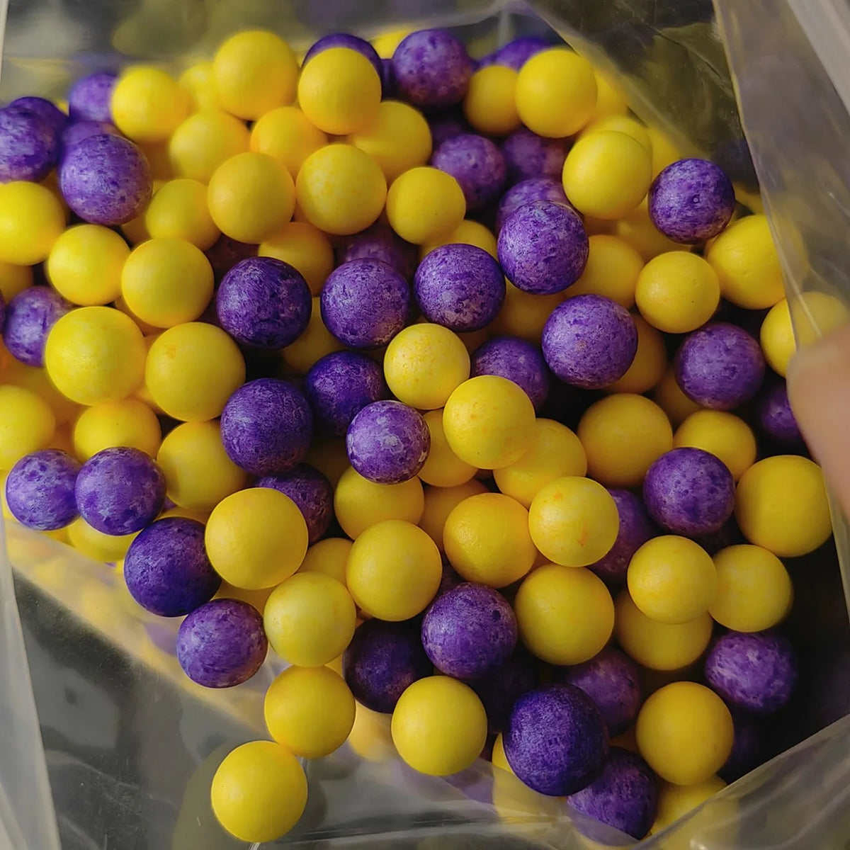 A clear bag filled with yellow and purple foam beads for crafting and decoration.