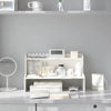 A white two-layer desktop organizer shelf displaying various skincare and beauty products.