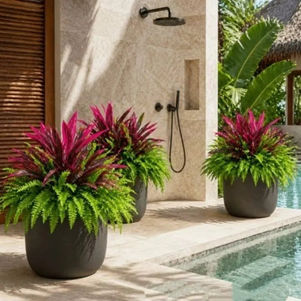 A potted artificial Dracaena Boston fern with vibrant pink and green leaves sits on a patio next to a swimming pool.