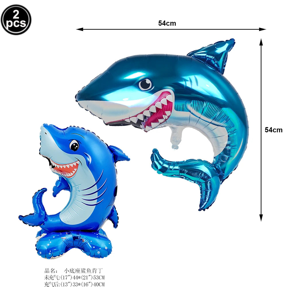 A shiny blue shark foil balloon is shown, with a smaller version also visible, used for ocean-themed party decoration.