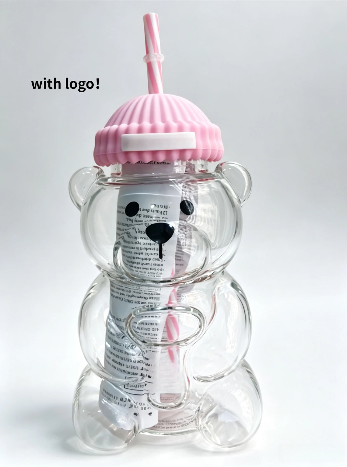 A clear glass coffee cup with a pink lid and handle, featuring a white label.