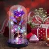 A crystal rose flower with butterfly wings is illuminated inside a glass dome on a wooden surface.