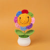 Hand woven crochet flower in vibrant colors with green leaves potted in a white ceramic cup