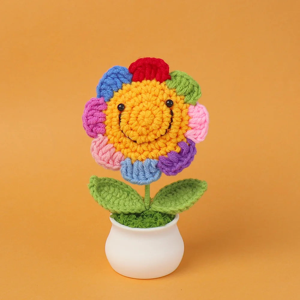 Hand woven crochet flower in vibrant colors with green leaves potted in a white ceramic cup