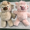 A pair of fluffy plush toys, one brown and one pink, resembling West Highland calves.