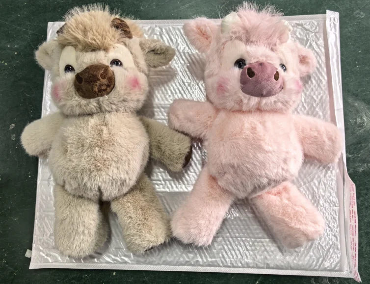 A pair of fluffy plush toys, one brown and one pink, resembling West Highland calves.