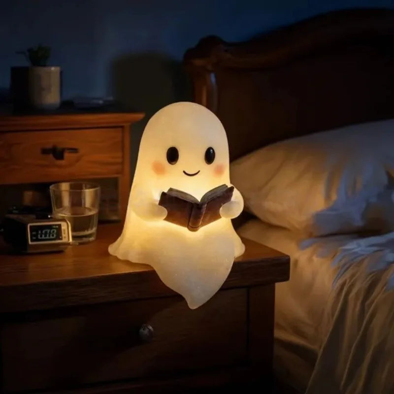 A cute ghost night light shaped like a glowing figure reading a book on a wooden bedside table.