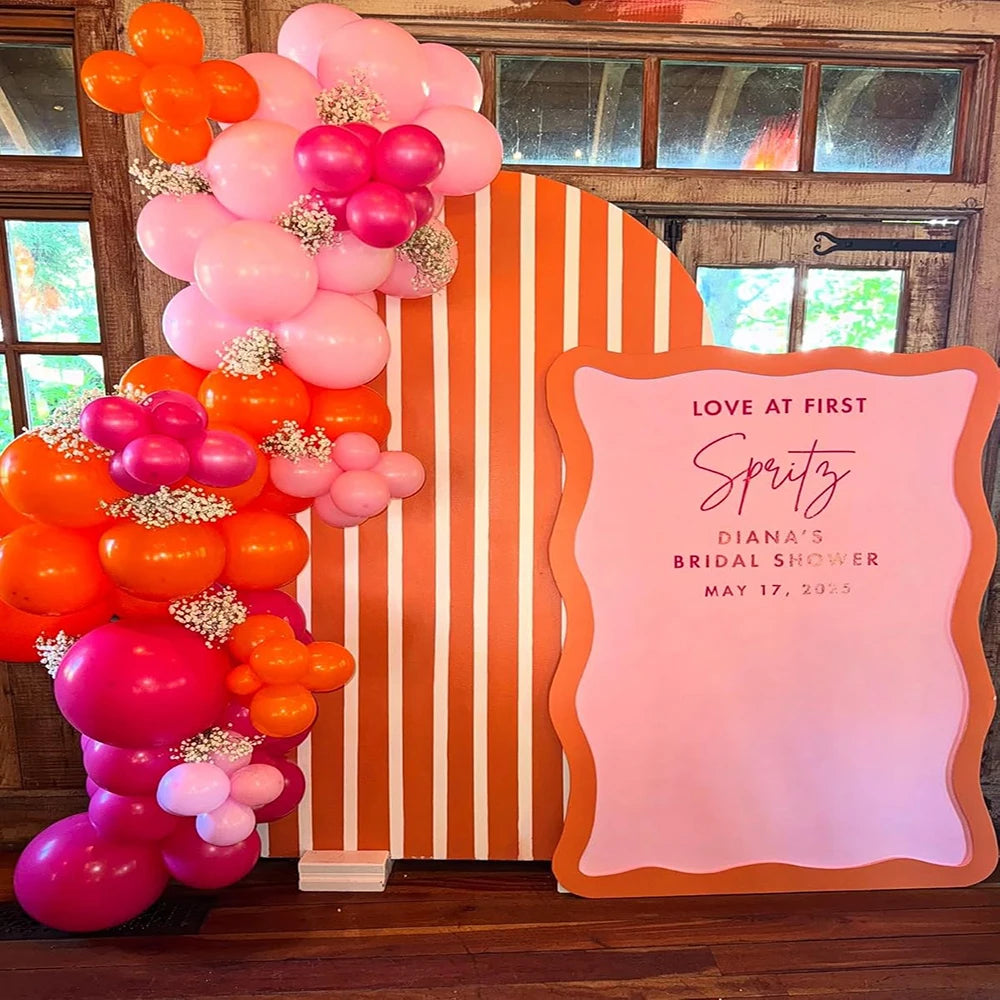 A display featuring a balloon garland in pink and orange colors against a striped background with a sign for a bridal shower.
