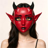 A woman wearing a red horned fantasy creature mask with black eyeliner and gold accents.