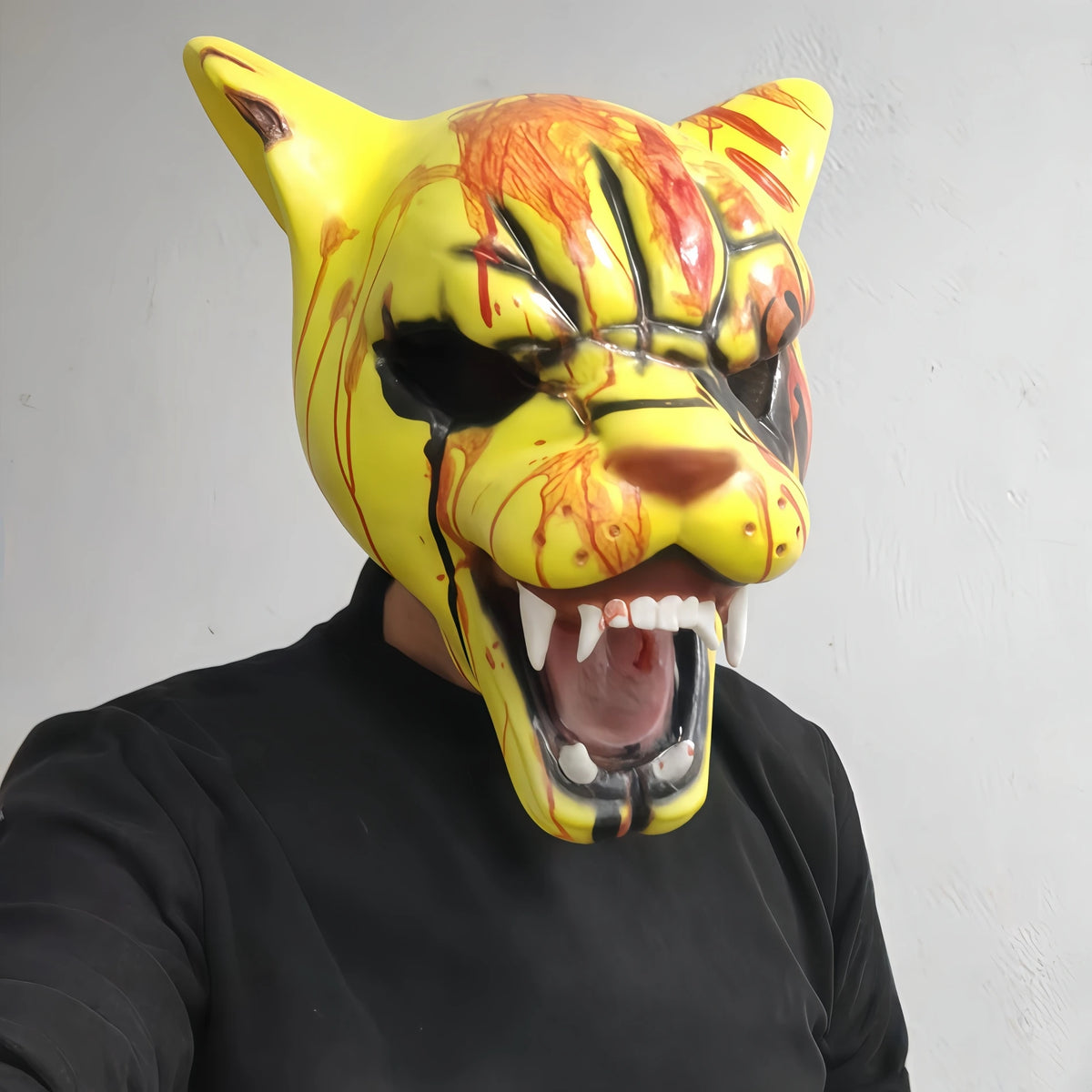 A yellow and orange latex mask resembling a tiger's head with blood effects, worn by a person.